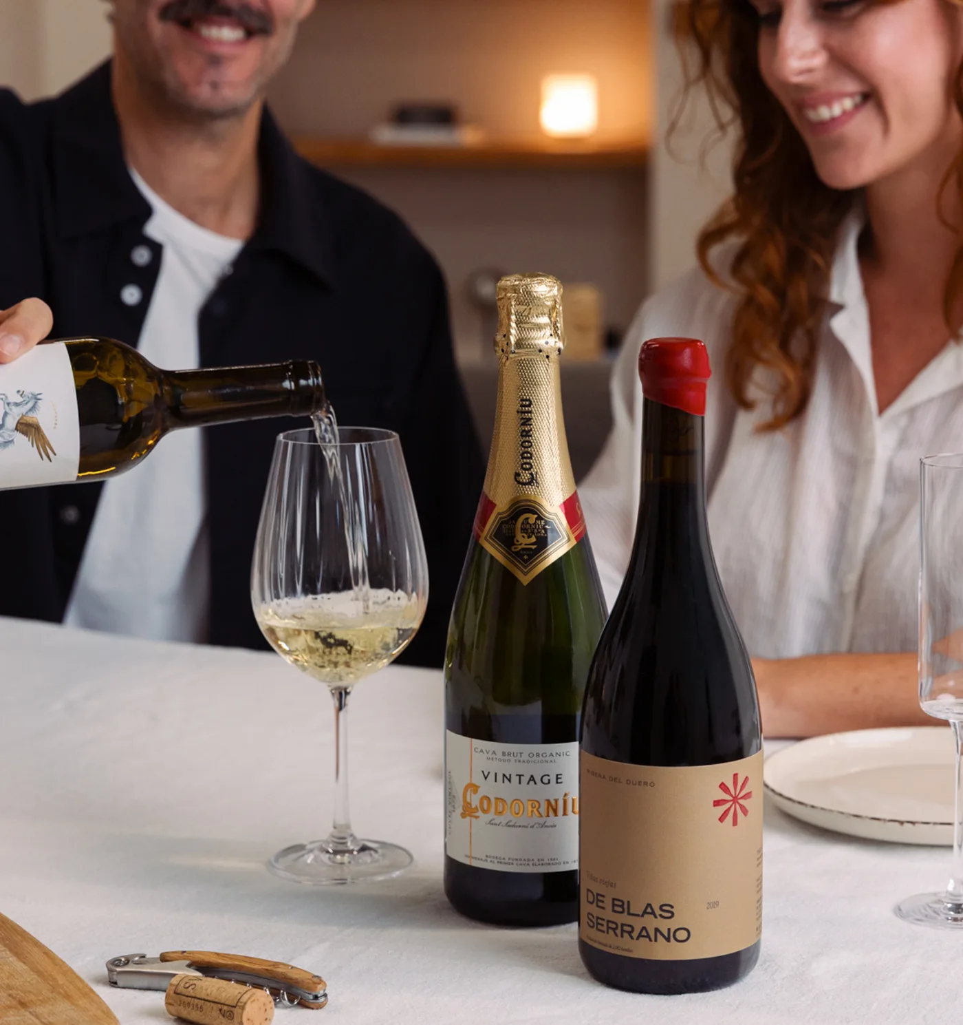 Parella brindant amb vi blanc, cava i negre a taula