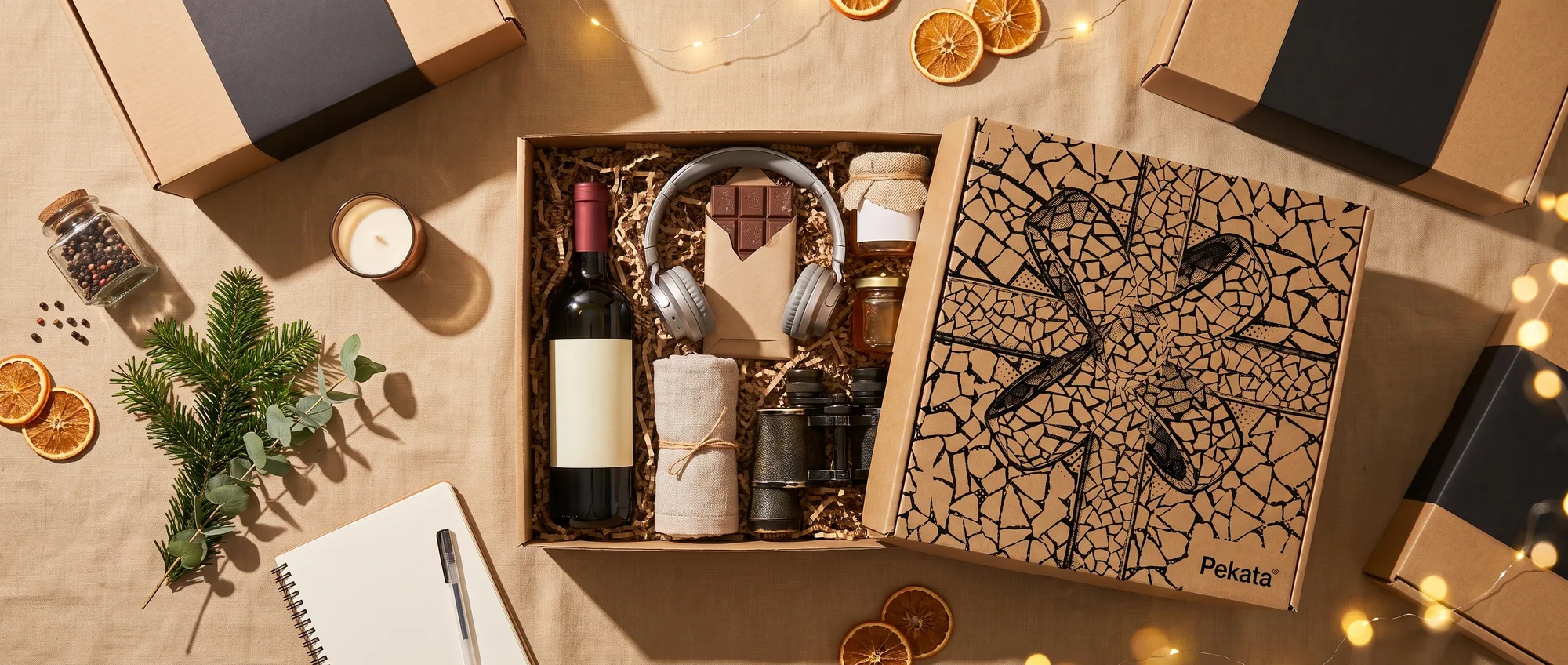 Vista cenital de una caja de Navidad Pekata abierta rodeada de distintas ideas de regalo: vino, auriculares, chocolate y una vela