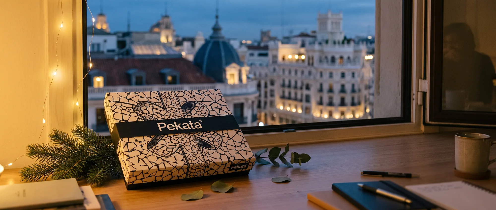 Caja de lote de Navidad Pekata junto a una ventana con la Gran Vía de Madrid iluminada al fondo