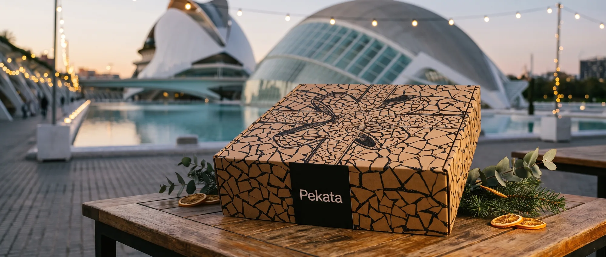 Caja de Navidad Pekata cerrada sobre una mesa con la Ciudad de las Artes y las Ciencias de Valencia desenfocada al fondo