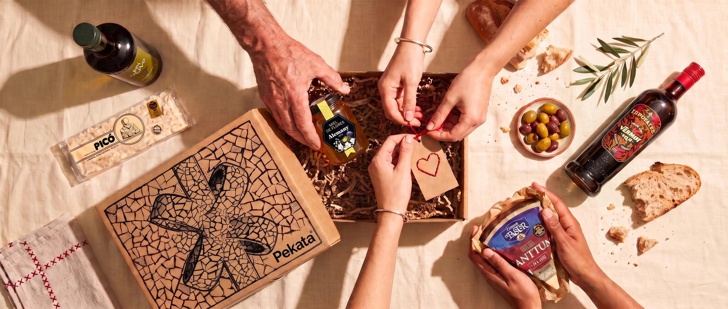 Manos de varias personas preparando una caja Pekata con una etiqueta kraft con un corazón cosido